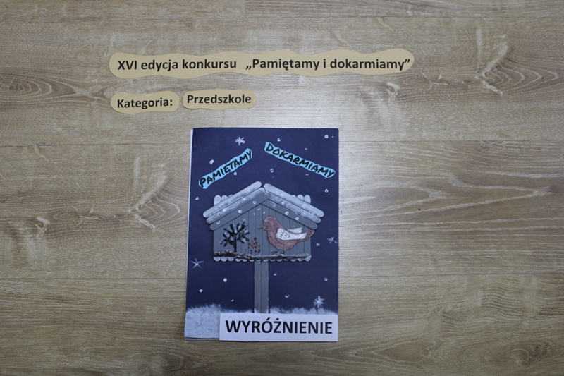 Zdjęcie przedstawia pracę, ktora otrzymała wyróżnienie w kategorii przedszkole. Karmnik zrobiony z patyczków, a w środku ptak z papieru.