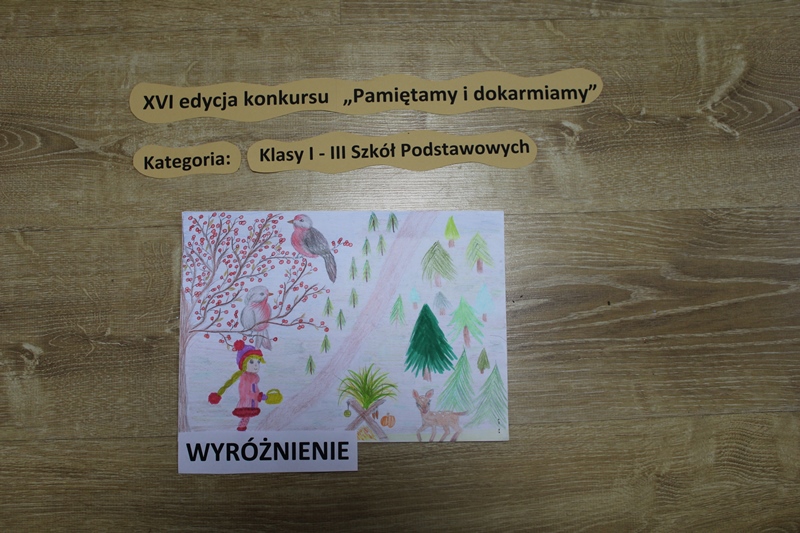 Zdjęcie przedstawia pracę, ktora otrzymała wyróżnienie w kategorii klasy I-III szkoły podstawowej, rysunek dziewczynki, która dokarmia zwierzęta w lesie.