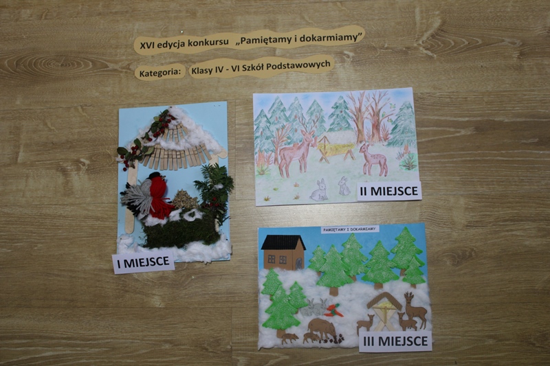 Zdjęcie przedstawia prace laureatów konkursu w kategorii klasy IV-VI szkoły podstawowej. I miejsce karmnik zrobiony z użyciem naturalnych materiałów i ptaka z włóczki. II miejsce rysunek zwierząt leśnych przy paśniku. III miejsce praca z użyciem różnych materiałów przedstawia zwierzęta leśne przy paśniku.