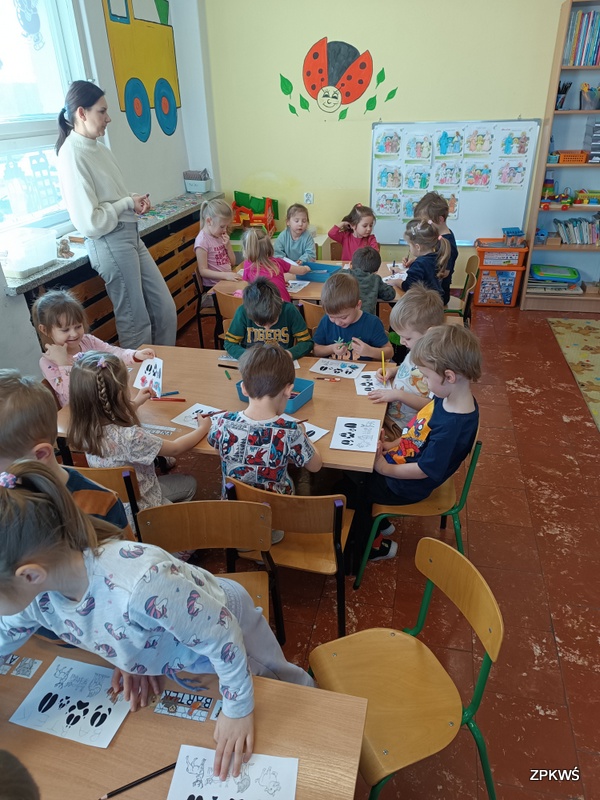 Grupa dzieci siedząca przy stolikach koloruje kolorowanki