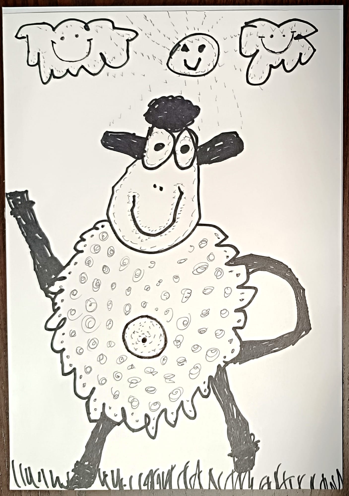 Na rysunku znajduje się uśmiechnięta owca narysowana czarnym markerem. Owca ma duże oczy, czarną grzywkę i puchate futerko ozdobione spiralnymi wzorkami. Stoi na trawie, z jedną nogą uniesioną do góry, jakby machała. Nad nią świeci słońce z uśmiechniętą buzią, a po jego bokach widnieją dwa obłoczki w kształcie napisów z uśmiechami. 