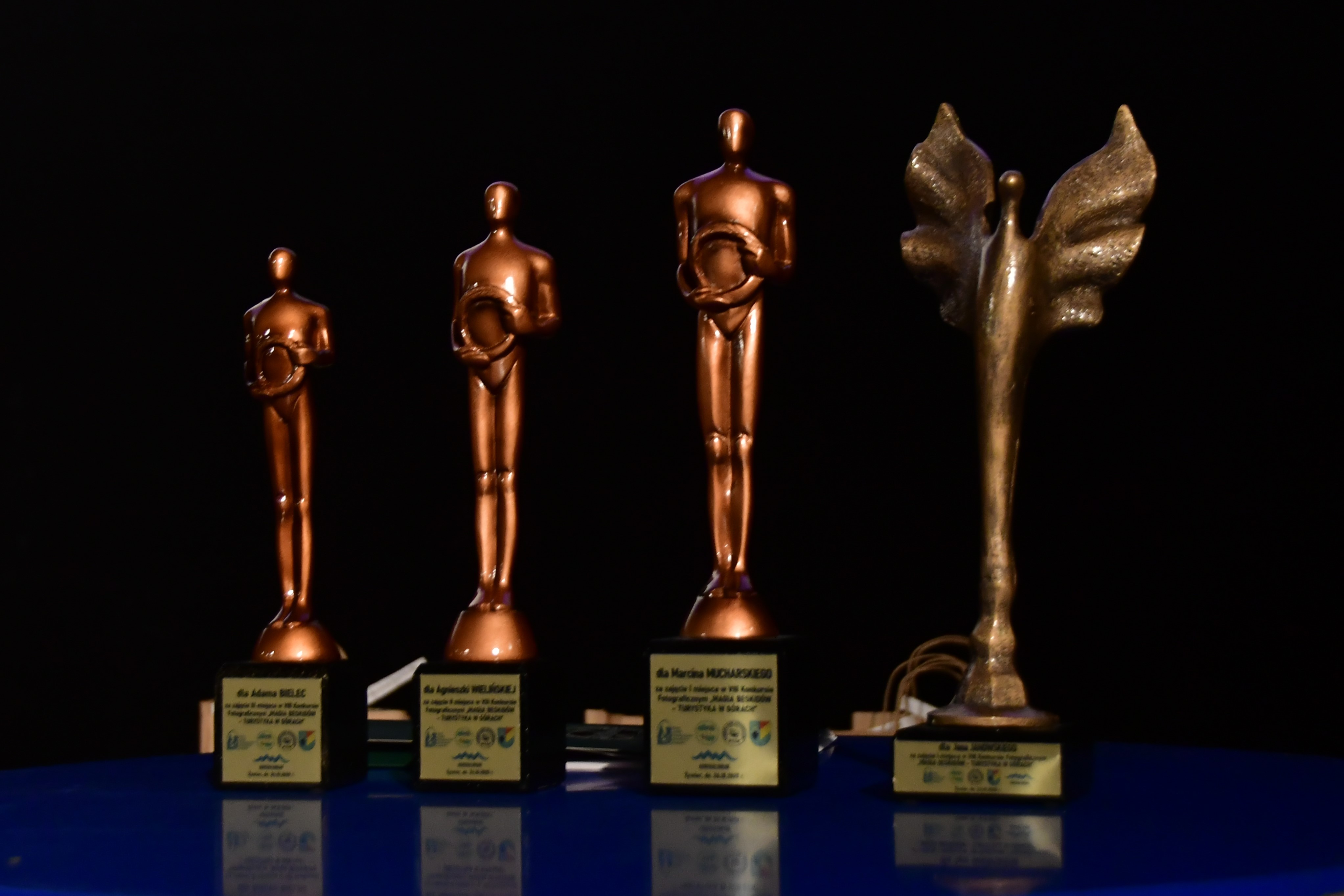 Cztery statuetki dla laureatów konkursu. Statuetki w kolorze złotym z tabliczkami z imionami i nazwiskami laureatów.