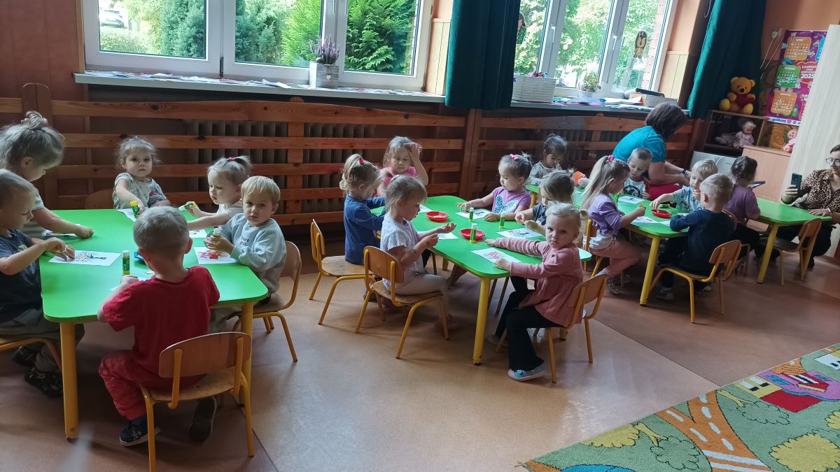 Przedszkolaki siedzą przy stolikach i kolorują drzewa na kartce