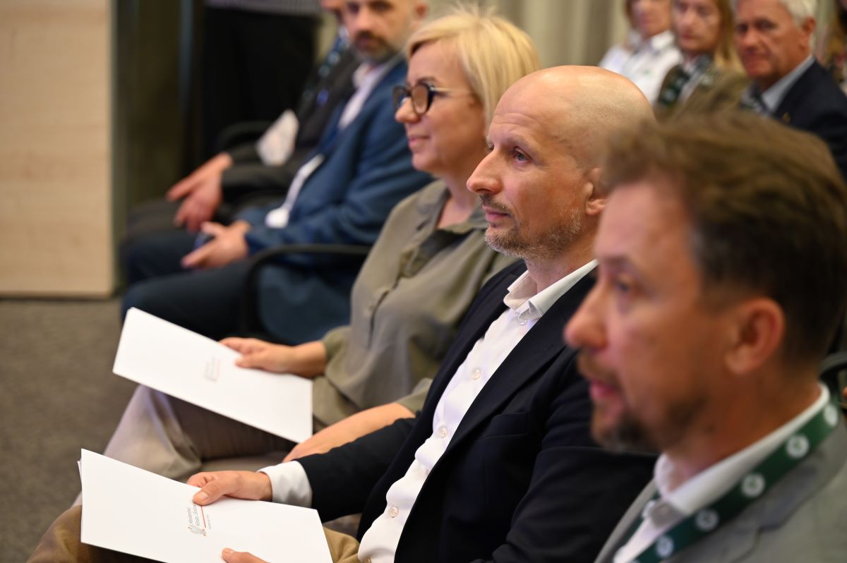Uczestnicy konferencji z okazji 50 – lecia parków krajobrazowych: Minister Klimatu i Środowiska Paulina Hennig – Kloska, Główny Konserwator Przyrody Mikołaj Dorożała i Generalny Dyrektor Ochrony Środowiska Piotr Otawski siedzą obok siebie i przysłuchują się prelegentom konferencji.