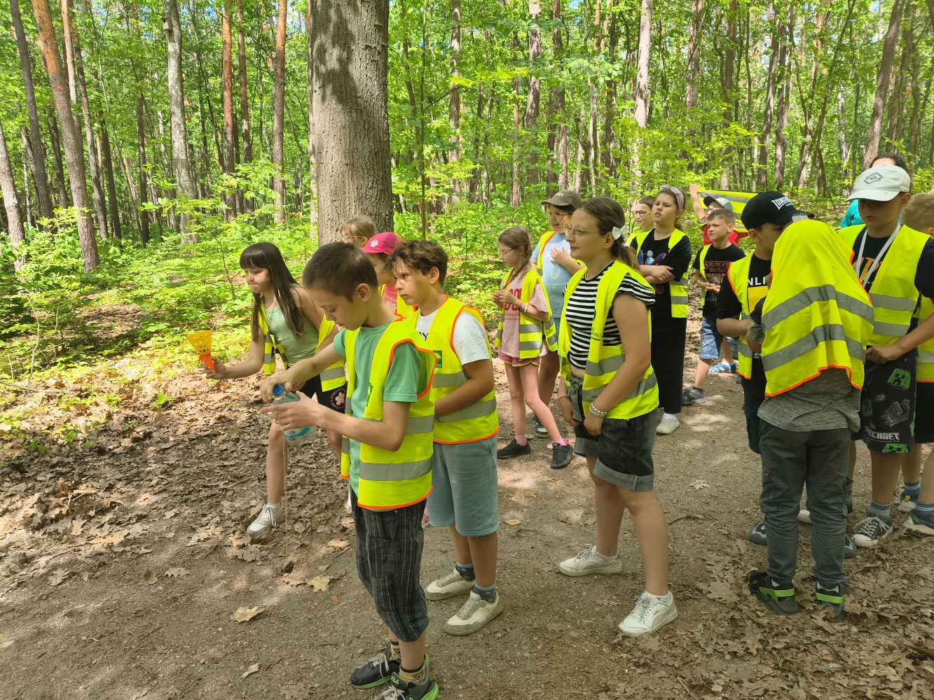 Grupa dzieci w lesie podczas gry terenowej.