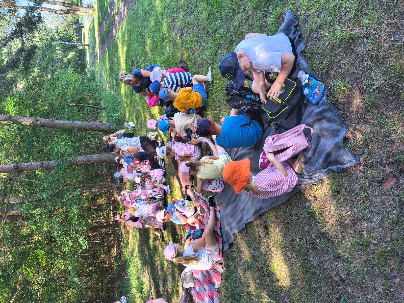Dzieci siedzą na kocach podczas pikniku przy stawie.