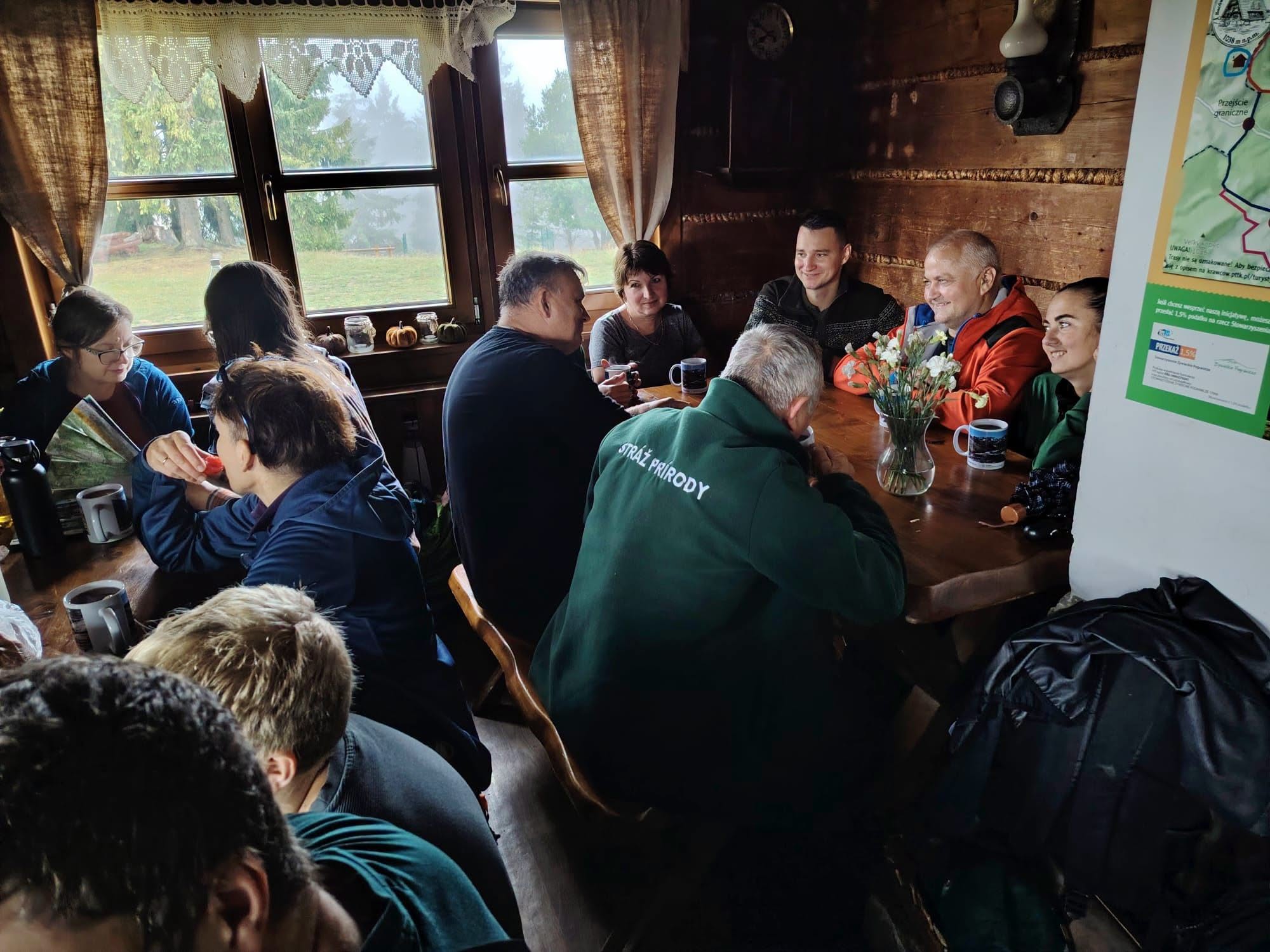 Grupa osób siedzi w schronisku przy stołach.